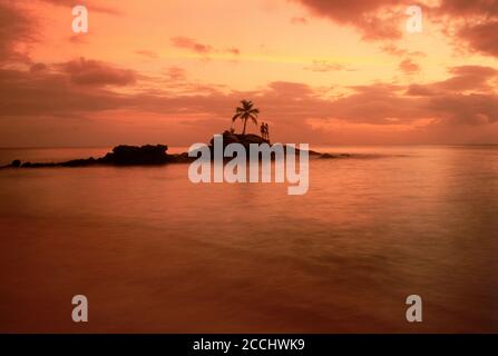 Couple on rocky point with one palm tree off Mahe Island in Seychelles at sunset Stock Photo