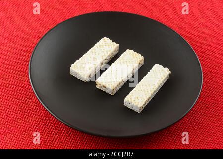 White chocolate covered wafer cookies with cocoa cream on black plate on red tablecloth Stock Photo