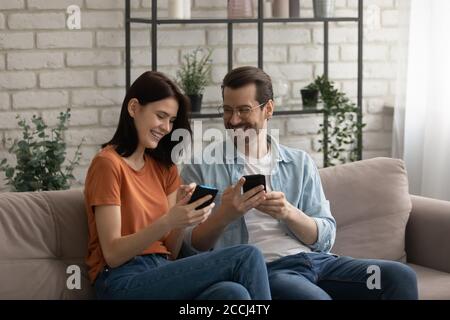 Happy millennial couple relax on sofa using cellphones Stock Photo