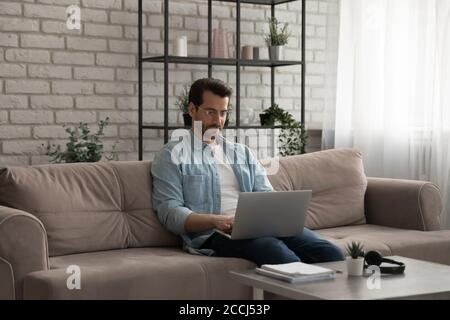 Caucasian man sit on couch working on laptop at home Stock Photo