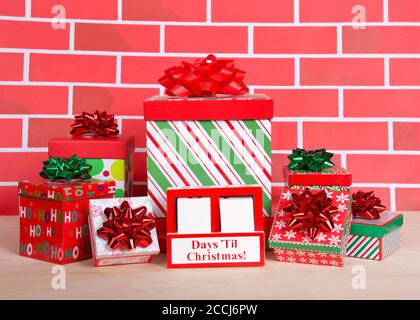 How many days til Christmas white wood blocks in a red box with presents stacked around it sitting on a light wood table with cartoonish brick wall ba Stock Photo