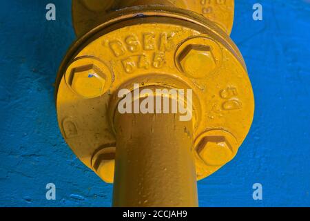 A close up view of a large yellow industrial cast iron pipe connection against a blue stone background. Stock Photo