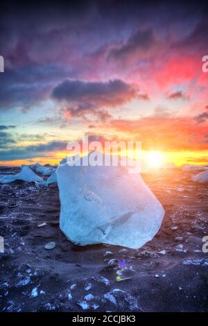 Beautiful sunset over famous Diamond beach, Iceland. This sand lava beach is full of many giant ice gems, placed near glacier lagoon Jokulsarlon. Stock Photo