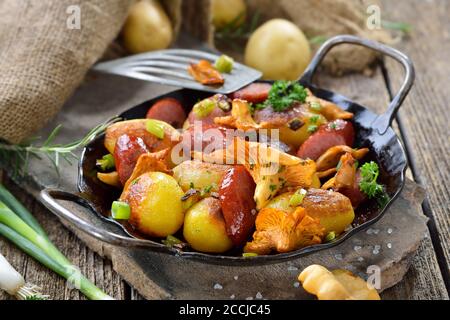 Fried potatoes with fresh chanterelles and sliced cabanossi sausages served in an iron pan with rustic ambience Stock Photo