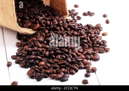 a collection of roasted coffee beans in a crochet bag on a white wooden plinth. Roasted coffee beans scattered of the burlap bag isolated on white Stock Photo
