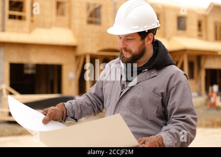 Builder looking at architectural drawing plan on paper at construction site. Stock Photo