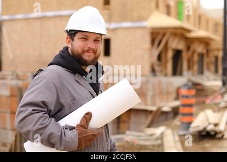 Caucasian builder holding architecture drawing plan on paper at construction site. Stock Photo