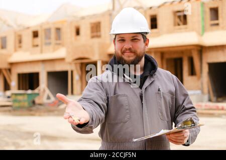 Bearded builder giving apartment keys and holding drawing plan in notebook. Stock Photo