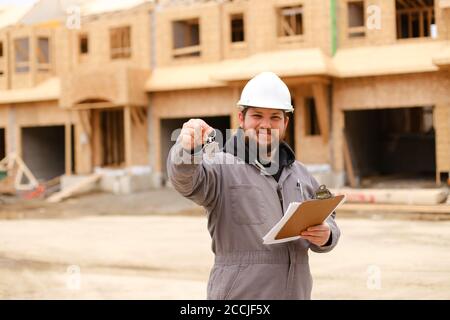 American builder giving apartment keys and holding drawing plan in notebook. Stock Photo