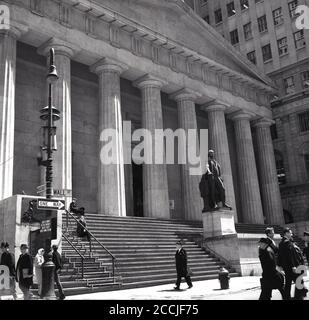 1960s, historical, exterior view of the grand columned US treasury building, known as Federal Hall at 26 Wall St, New York City, NY, USA, with the statue of George Washington at the front. The historic building originally opened in 1703 and then the current Greek Revival-style building was completed in 1842. At 26 Wall st, the building is in the heart of Manhattan's financial district. George Washington was sworn in as President there, and it was where the US Bill of Rights was written, Stock Photo