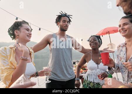 Group of happy young people talking to each other and laughing while having fun at a party outdoors Stock Photo