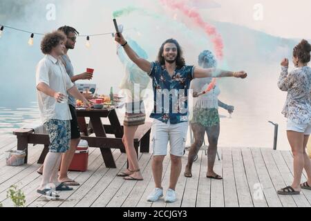 Portrait of young man smiling at camera while standing on a pier and dancing among his friends Stock Photo