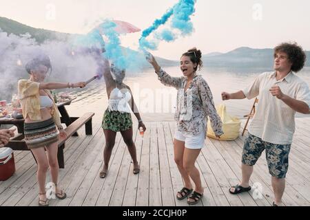Group of teenagers dancing on a pier outdoors among colored smoke Stock Photo
