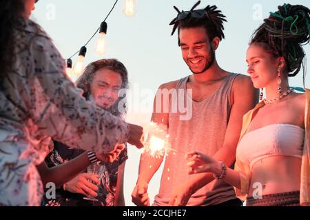 Group of young people standing in circle and lighting sparklers during the party Stock Photo