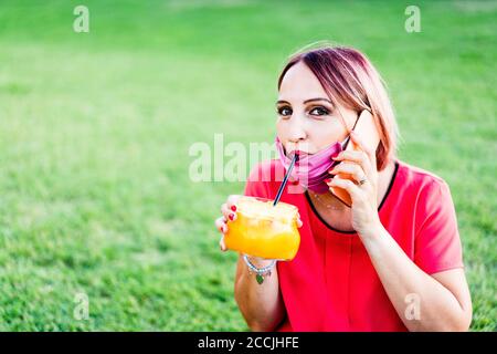 Woman with red lipstick and rose dyed hair drinking orange juice from retro bottle outdoor - Drinking summer cocktail - freshly squeezed orange - Heal Stock Photo