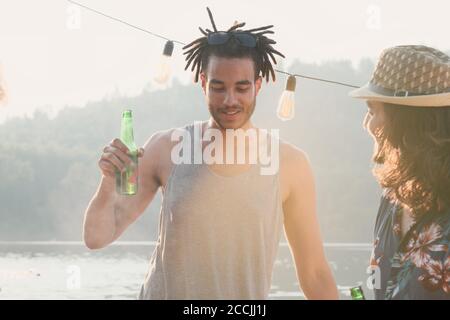 Young man drinking beer from the bottle and talking to his friend while they standing outdoors Stock Photo