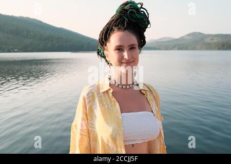 Portrait of young woman with fashion hairstyle looking at camera with beautiful view of the lake behind her Stock Photo