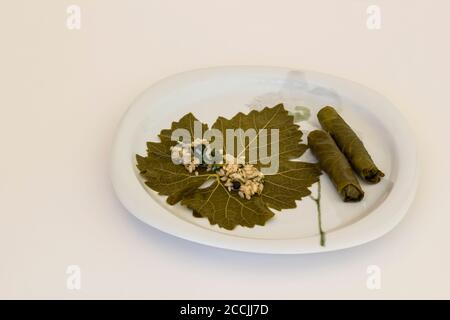 Hand is wraps,rolling of wet grape leaves in white plate,Traditional Turkish Food preparation,above view Stock Photo