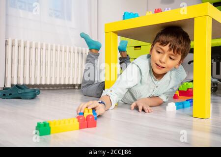 Boy play with blocks under table in kids room laying on the floor Stock Photo