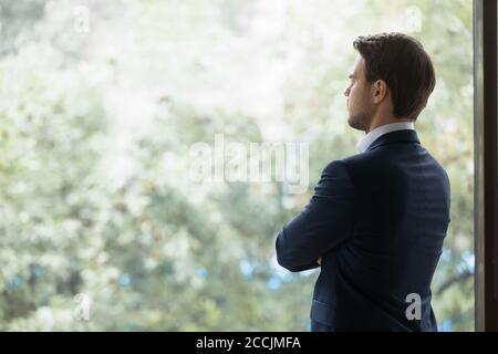 Back view of young thoughtful businessman standing near office window Stock Photo