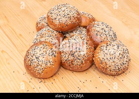 stack of small brown breads with white and black sesame on wooden table, used for burgers Stock Photo