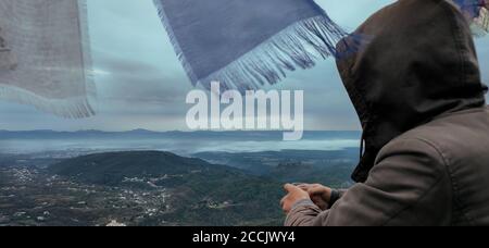 Travel portrait of man wearing hoodie with  face hidden looking towards the mountains Stock Photo