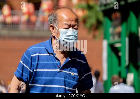 Elderly Chinese man walking on street wearing surgical face masks, London, UK Stock Photo