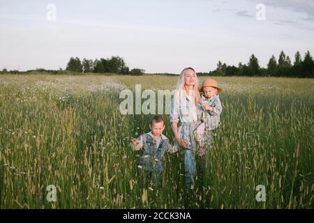 Smiling mother with two children walking on field Stock Photo