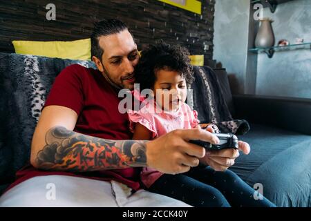 Father with daughter playing video game while relaxing on sofa at home