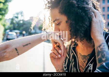 Close-up of loving man with curly hair kissing on girlfriend's hand in city Stock Photo