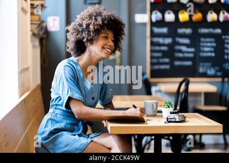 Thoughtful woman writing in book while sitting at table in coffee shop Stock Photo