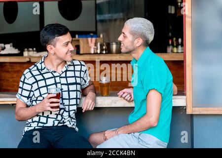 Smiling gay couple talking while drinking beer at bar counter Stock Photo