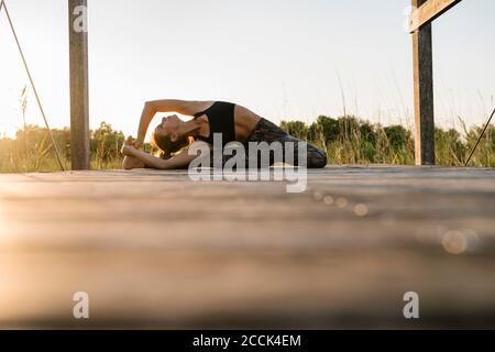 Young athlete practicing lizard pose on pier at countryside Stock Photo