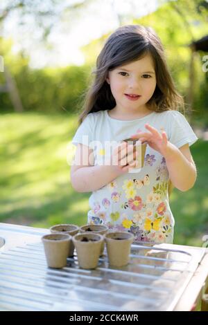 Cute girl planting seeds in small pots on table at yard Stock Photo