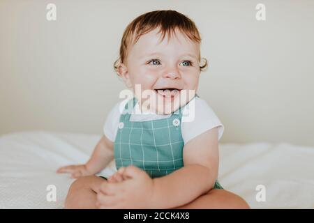 Close-up of cheerful baby girl looking away while sitting on bed at home Stock Photo