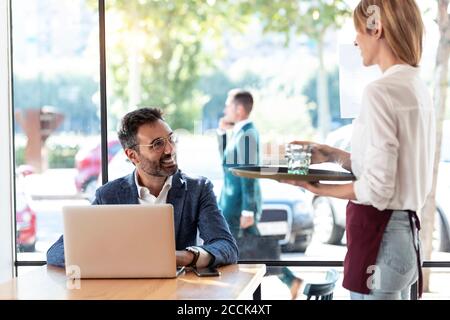 Smiling businessman looking at waitress holding glass of water in restaurant Stock Photo