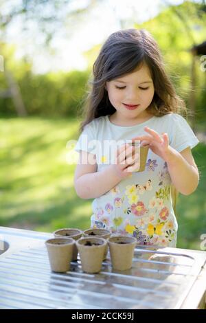 Cute girl planting seeds in small pots on table at garden Stock Photo