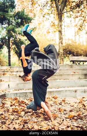 Male friends jumping upside down in public park Stock Photo