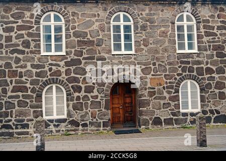 Old stony building with windows. Wall made out of big stones. Old building material concept. Ancient stony house or part of defenses. Building with thick walls and heavy wooden front door. Stock Photo