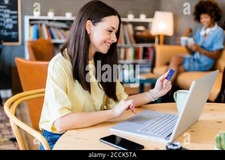 Happy woman using credit card and laptop while shopping online in cafe Stock Photo