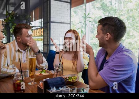 friends are playing together who I am in cafe, leisure time. humour, entertainment concept Stock Photo