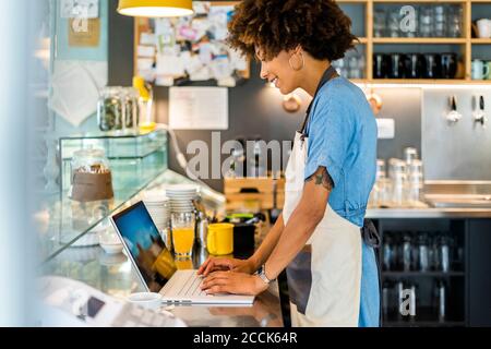 Female owner using laptop at counter in coffee shop Stock Photo