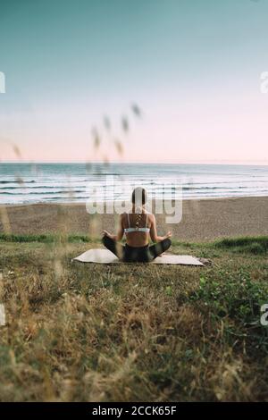 Young woman meditating at beach against clear sky during sunset Stock Photo