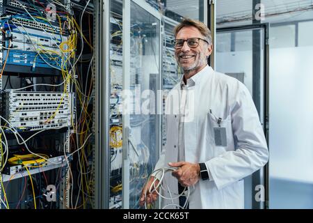 Male IT professional holding cables standing by network server in date center Stock Photo