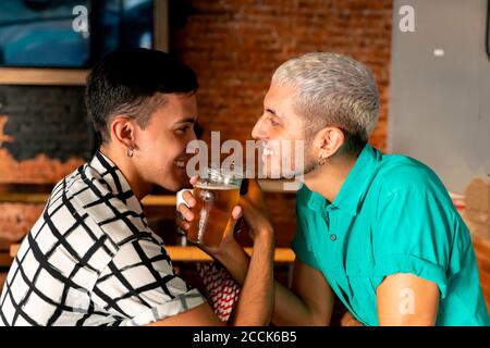 Romantic gay couple enjoying drinking beer with arm in arm at bar Stock Photo
