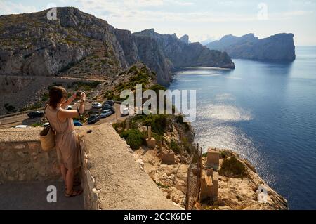 Young woman photographing the Majorcan coastline landscape from Formentor cape (Cap de Formentor, Majorca, Balearic Islands, Mediterranean sea, Spain) Stock Photo