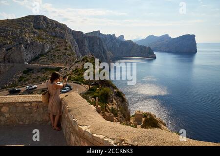 Young woman photographing the Majorcan coastline landscape from Formentor cape (Cap de Formentor, Majorca, Balearic Islands, Mediterranean sea, Spain) Stock Photo