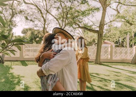Loving senior woman embracing granddaughter while standing against trees in yard Stock Photo