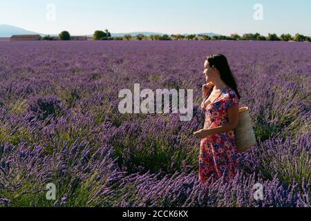 Portrait of beautiful woman standing in vast lavender field with basket in hand