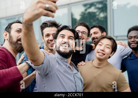 Cheerful man taking selfie with male friends while standing in city Stock Photo